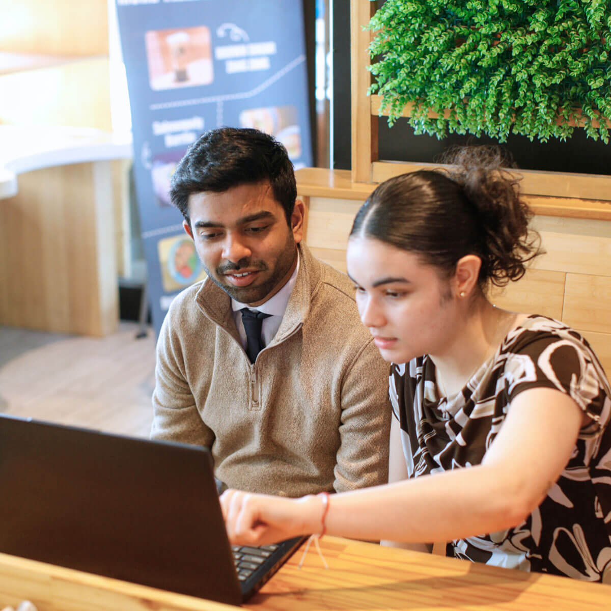 A man and a woman collaborate at a table with a laptop, representing teamwork at the University of Rochester Simon Business School.